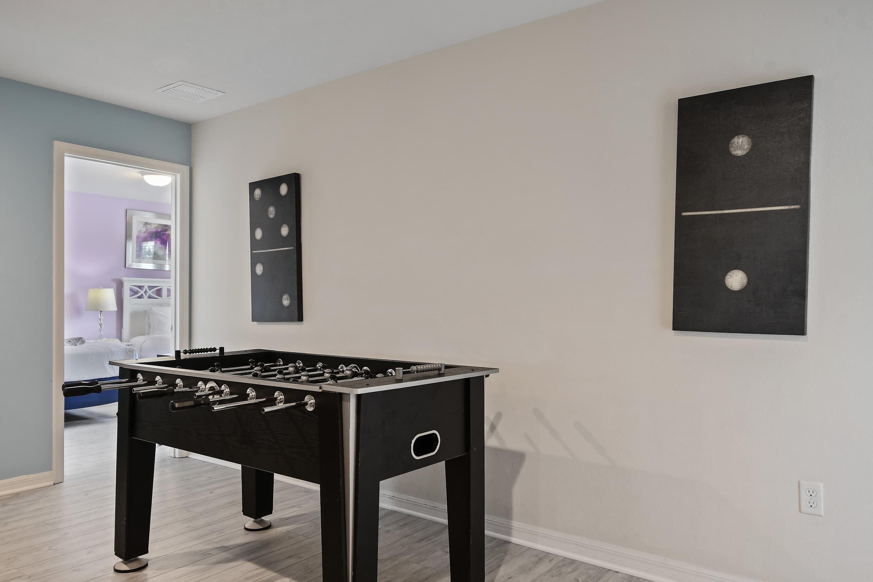 Une pièce avec une table de baby-foot, un mur blanc orné d’une œuvre d’art noire et une porte donnant sur une autre pièce.