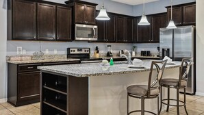 A modern kitchen with dark wood cabinets, stainless steel appliances, granite countertops, and pendant lighting. - Ultimate 8BR Family Fun in Resort Near Disney! (Kissimmee)