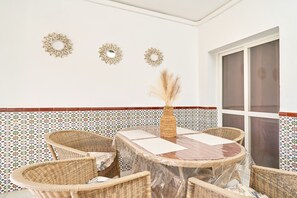 Un comedor con una mesa redonda, sillas de mimbre y espejos decorativos en la pared.