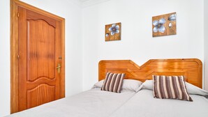 A bedroom with a wooden door, two wall-mounted flower paintings, a wooden headboard, and two striped pillows. - 'Animas 1' Apartment with Balcony, Wi-Fi, and Air Conditioning (Nerja)