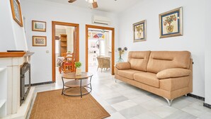 A living room with a beige sofa, a fireplace, a ceiling fan, and framed artwork on the walls. - 'Animas 1' Apartment with Balcony, Wi-Fi, and Air Conditioning (Nerja)