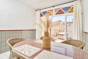 Un balcon agrémenté de meubles en osier, une table avec un chemin de table aux motifs géométriques et un vase contenant des plantes séchées.