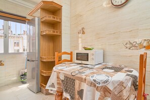 Une cuisine équipée d’un four à micro-ondes, d’un réfrigérateur, d’une étagère en bois et d’une table recouverte d’une nappe à motifs.