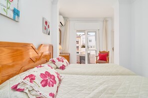 Une chambre avec deux lits, une tête de lit en bois, une table de chevet et une vue sur l’extérieur, visible à travers une porte vitrée.