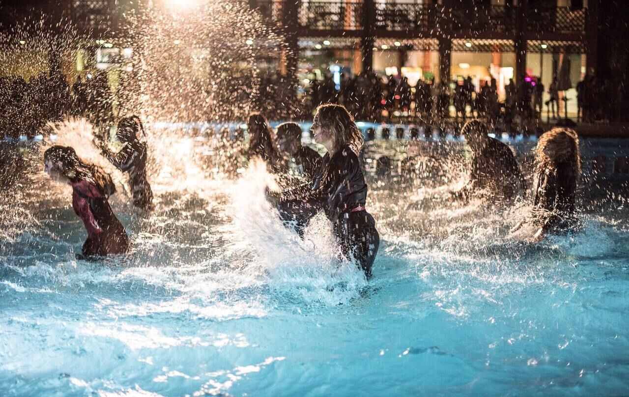 A group of people playing in a water fountain at night.