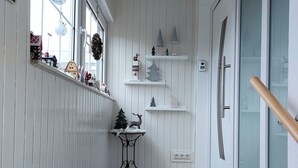 Valoisa käytävä, jonka seinät on verhoiltu valkoisilla paneeleilla, pieni pöytä koriste-esineineen ja lasiruutullinen ovi.