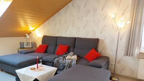Tunnelmallinen olohuone, jossa on harmaa sohva, punaiset koristetyynyt, pieni pöytä ja kynttilä sekä lattiavalaisin.