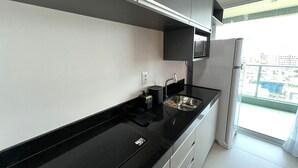 Una cocina moderna con encimera negra, armarios blancos y un lavamanos de acero inoxidable.
