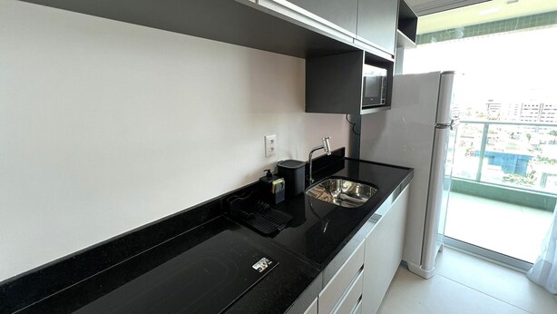 A modern kitchen with a black countertop, white cabinets, and a stainless steel sink. - RN STUDIO APTO 508 (Maceió)