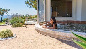 Una persona descansando junto a una piscina con vista al mar y un jardín de cactus.