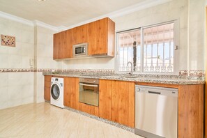 A kitchen with wooden cabinets, a microwave, a washing machine, an oven, and a dishwasher. - Duplex Home Next to Balcón de Europa with 2 Large Sunny Terraces and Barbecue (Nerja)