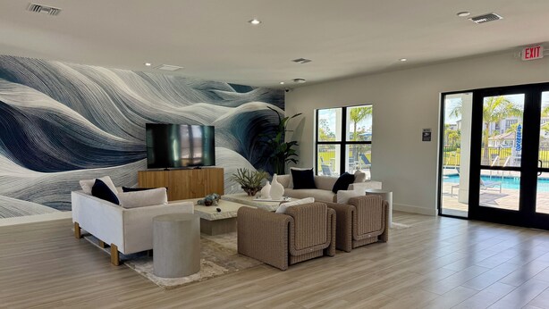 Un vestíbulo moderno con un mural grande en la pared, un televisor de pantalla plana y una zona de estar con sofás y sillones de mimbre.