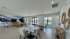 Amplio espacio interior con un gran mural, vista a la piscina y comedor con mesas y sillas.