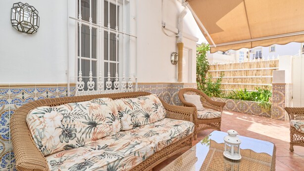 Ein Korbusofa mit Blumenmuster, ein Korpusfauteuil, ein kleiner Tisch mit einer Laterne und eine Wand mit geometrischem Fliesenmuster.