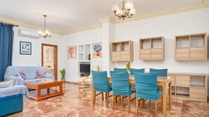 Ein Wohnzimmer mit Sofa, Couchtisch, Esstisch mit Stühlen, Wandregalen und einer Chandelier.