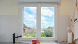 A kitchen with a window, a sink, a kettle, and a towel rack.