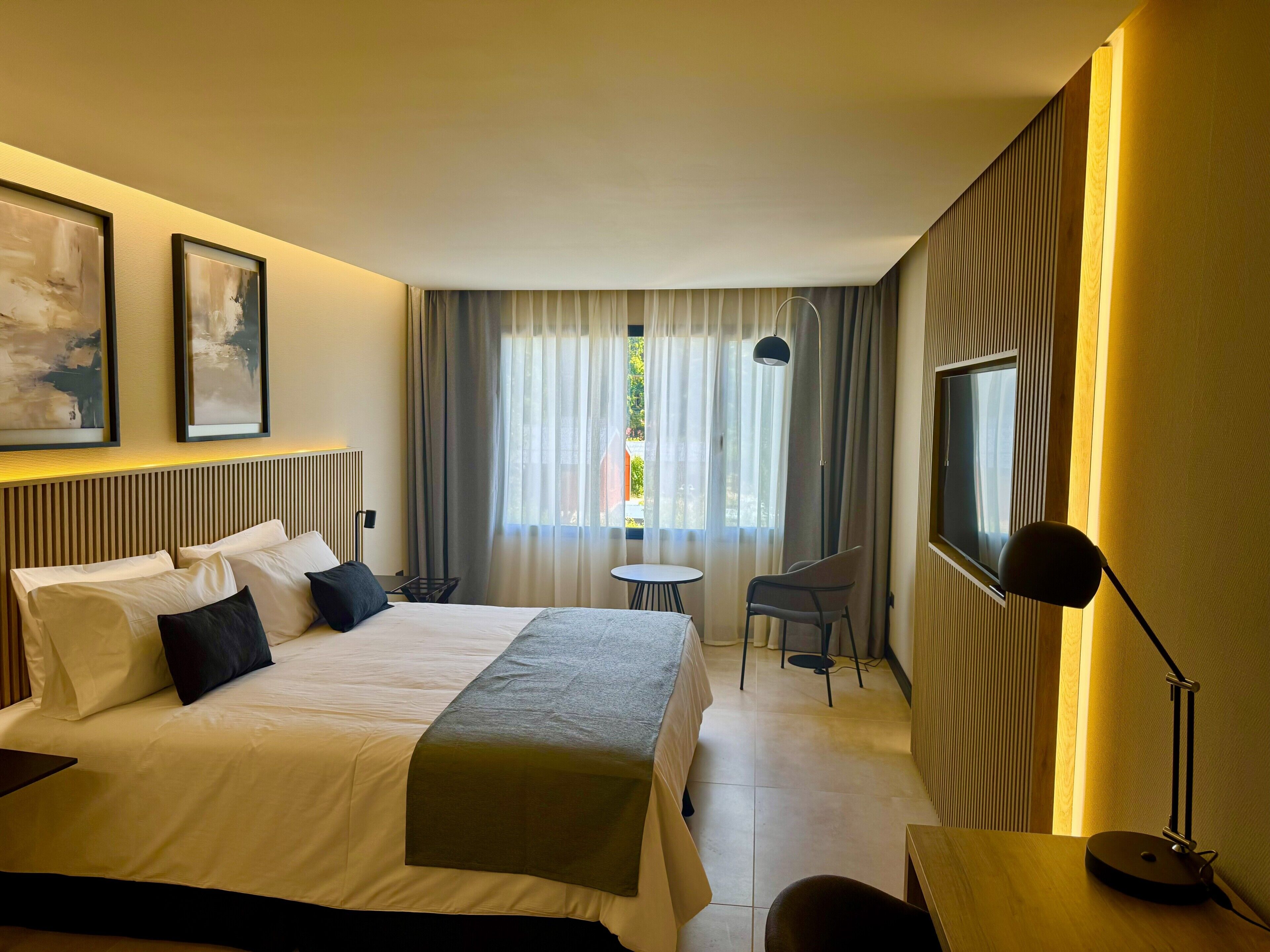 A hotel room with a bed, a desk, a chair, a TV, and a window with curtains.
