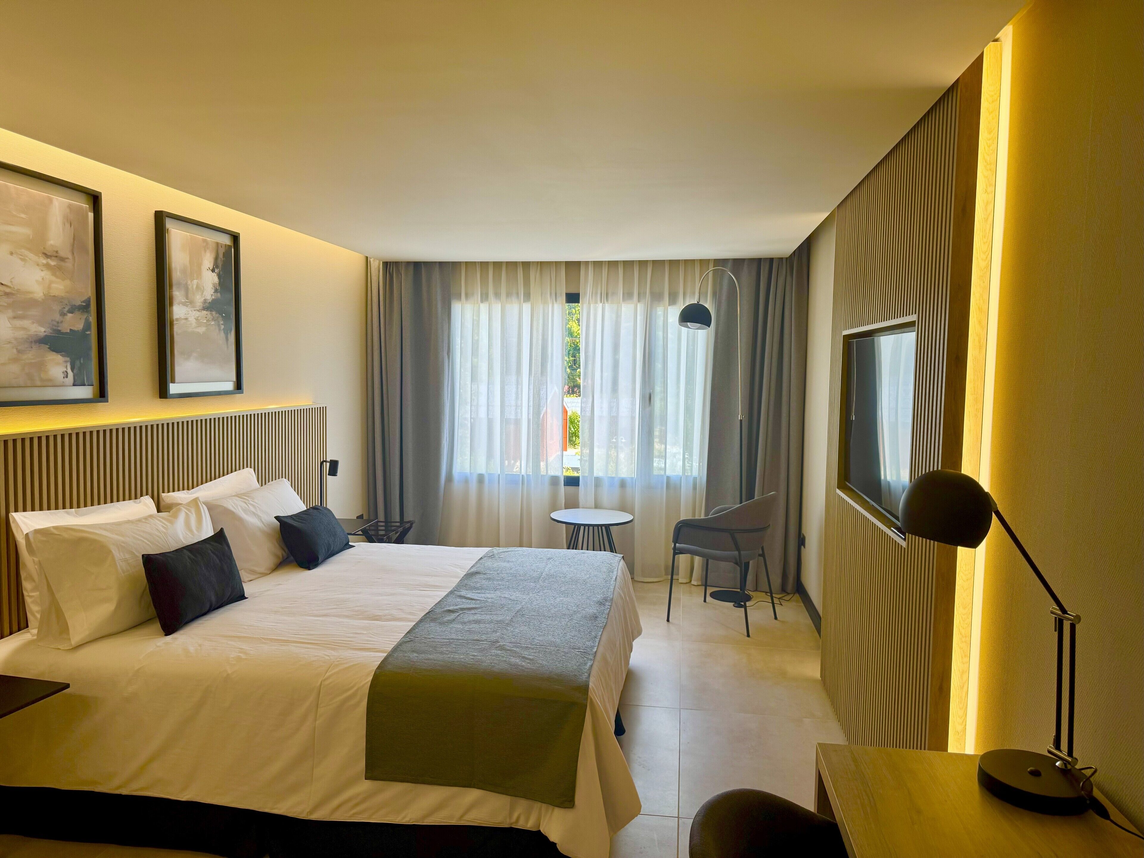 A hotel room with a bed, a desk, a chair, a TV, and a window with curtains.