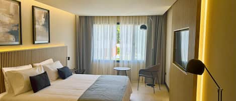 Una habitación de hotel con cama, escritorio, silla, televisor y ventana con cortinas.