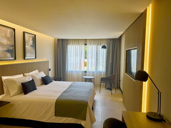Una habitación de hotel con cama, escritorio, silla, televisor y ventana con cortinas.