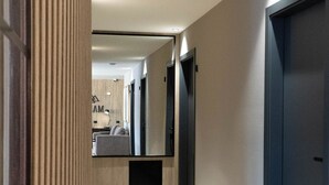 A modern hotel hallway with a wooden accent wall, a flat-screen TV, and a dark door. - MABRA SUITES (El Calafate)