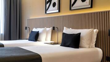 Habitación de hotel con dos camas, cada una con ropa blanca y almohadas negras. En la pared, encima de las camas, hay obras de arte enmarcadas.