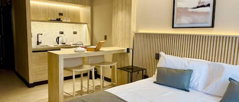 Una camera d'albergo moderna con angolo cottura, un letto con biancheria grigia e un quadro appeso al muro.