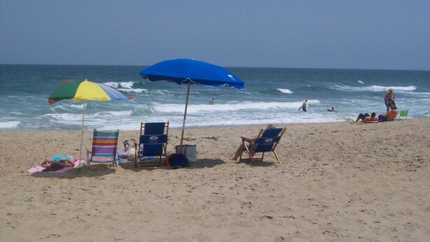 A beach with several beach chairs and umbrellas, a clear sky, and the ocean in the background. - Oceanfront paradise! Family-friendly condo with perfect unobstructed beach views (Kill Devil Hills)