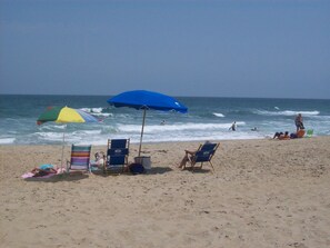 A beach with several beach chairs and umbrellas, a clear sky, and the ocean in the background.
