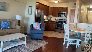 A modern living room with a sofa, a coffee table, and a dining area with a table and chairs. - Oceanfront paradise! Family-friendly condo with perfect unobstructed beach views (Kill Devil Hills)