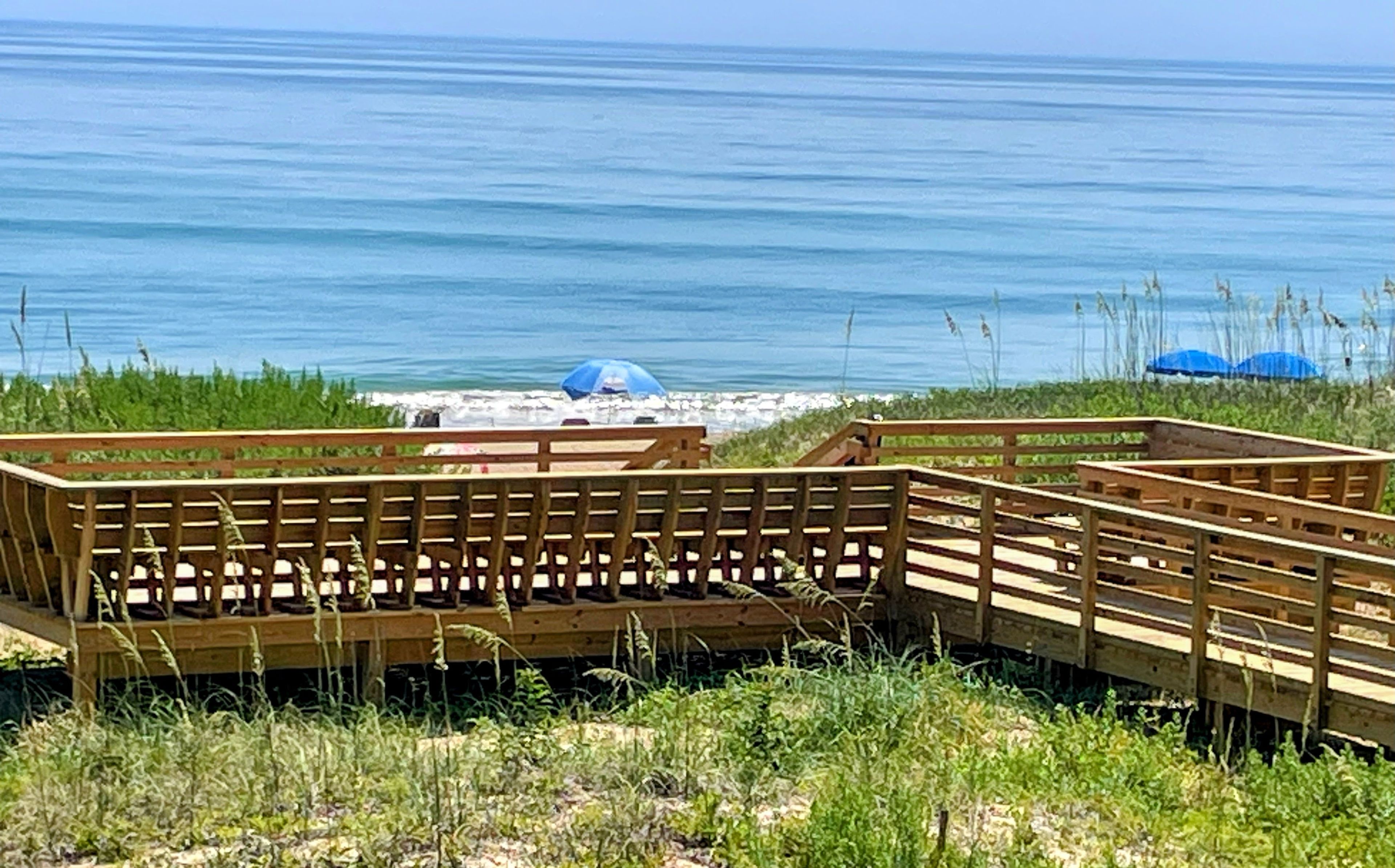 A wooden deck with benches overlooking a beach with umbrellas.