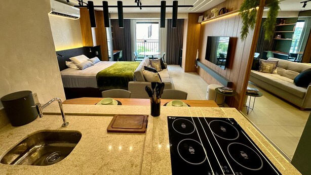 A modern hotel room with a kitchen area, a bed, a sofa, and a TV. - New and elegant studio in Campo Grande/MS (Centro Campo Grande)