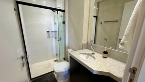 A modern bathroom with a glass-enclosed shower, a white toilet, a granite countertop sink, and a large mirror. - New and elegant studio in Campo Grande/MS (Centro Campo Grande)