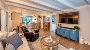 Un vaste salon comprenant un canapé en cuir, une table basse et un téléviseur fixé au mur. On y trouve également un coin repas avec des chaises et une table, ainsi qu’une cuisine équipée de placards, dont un placard bleu.