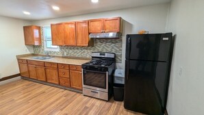 Una cocina con armarios de madera, un refrigerador negro, una estufa y un cubo de basura.