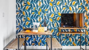 A modern living room with a patterned wallpaper, a wooden table with a bottle of wine, glasses, and cheese, and a flat-screen TV on a stand. - TBS 142 - Cosy Studio at the Gates of Paris (Paris)