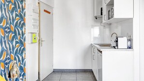 A narrow kitchen with white cabinets, a built-in oven, and a coffee maker. - TBS 142 - Cosy Studio at the Gates of Paris (Paris)