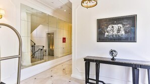 Un hall d’hôtel doté d’un sol en marbre, d’un escalier avec une rampe en verre, d’une console noire et d’une œuvre d’art encadrée accrochée au mur.