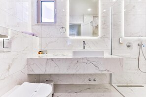 Ein modernes Badezimmer mit Marmorwaschbecken, einem Spiegel, einer Toilette und einer Duschkabine.