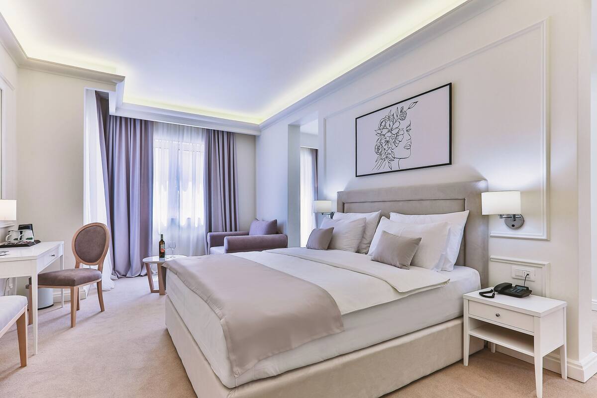 Ein Hotelzimmer mit einem großen Bett, einem Schreibtisch, einem Sessel, einem kleinen Tisch und einem Nachttisch mit einem Telefon.