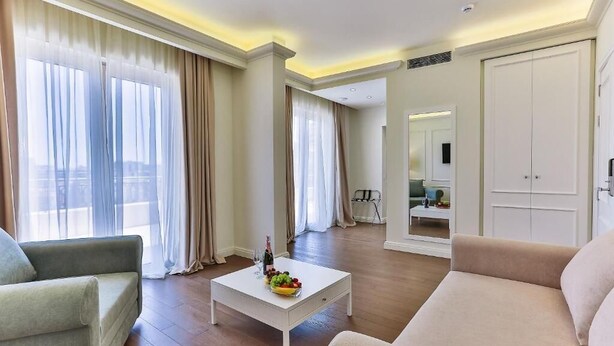 Un salon spacieux avec une table basse blanche, des canapés beige et de grandes fenêtres ornées de rideaux légers.
