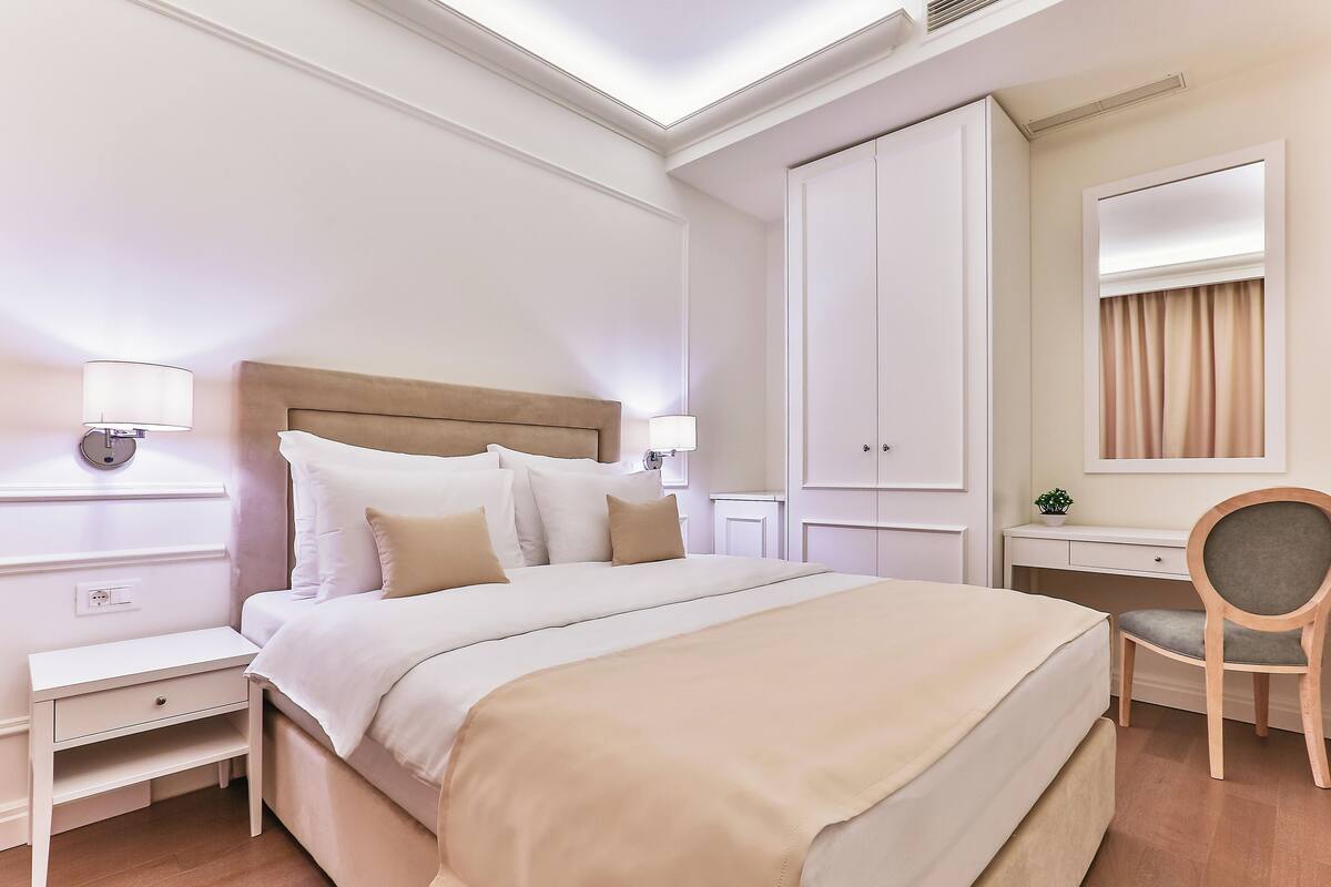 Ein ordentlich eingerichtetes Hotelzimmer mit einem großen Bett, Nachttischen, einem Schreibtisch und einem Sessel.