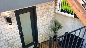 A wooden staircase leading to a door with a metal gate, a potted plant, and a stone wall. - Newly-built modern farmhouse condo available in Grosse Pointe Park! (Grosse Pointe Park)