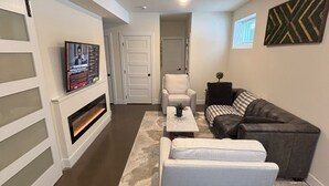 A modern living room with a fireplace, a sofa, a chair, and a television mounted on the wall. - Newly-built modern farmhouse condo available in Grosse Pointe Park! (Grosse Pointe Park)