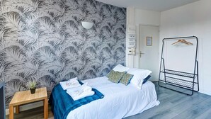 A bedroom with a bed, a bedside table with a plant, a hanging clothes rack, and a patterned wallpaper. - TheBlueStay 135 - Cosy apartment (Paris)