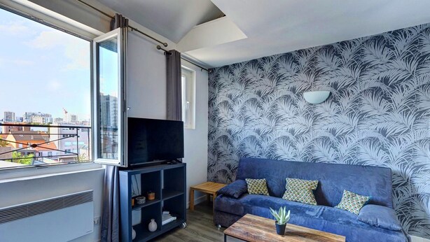 A modern living room with a sofa, a coffee table, a TV on a stand, and a patterned wallpaper. - TheBlueStay 135 - Cosy apartment (Paris)