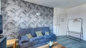 A modern living room with a grey sofa, patterned wallpaper, a wooden coffee table, and a black metal shelf unit. - TheBlueStay 135 - Cosy apartment (Paris)