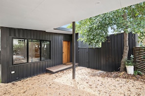 A modern house with a large window, a wooden door, and a gravel driveway.