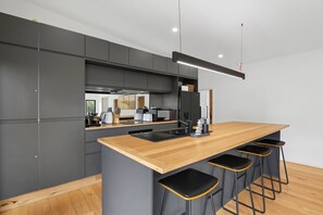 A modern kitchen with a central island, bar stools, and a view of the dining area. - Riverside Escape (Anglesea)