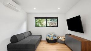 Quarto moderno com sofá cinzento, um pufe preto, um armário de madeira e uma TV na parede.